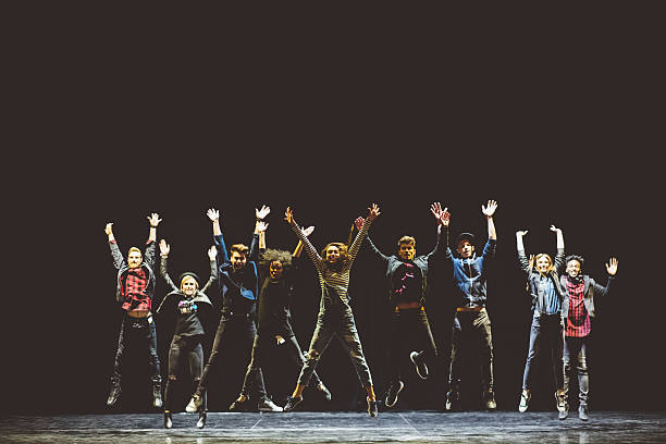 Group of young performers on the stage Group of young performers on the stage standing in the line, jumping with raised hands. Dark tones. stage theater stock pictures, royalty-free photos & images