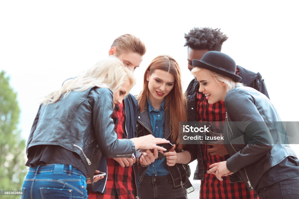 Multi ethnic group of friends using mobiles outdoors Multi ethnic group of happy young people using smart phones outdoors. 20-29 Years Stock Photo
