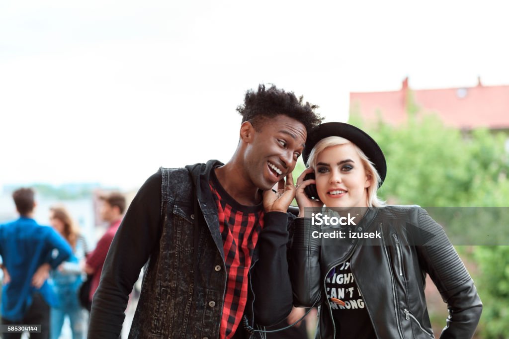 Afro american young guy and blonde girl using mobiles outdoor Afro american young guy and blonde girl using smart phones outdoor. Group of people in the background. Discussion Stock Photo