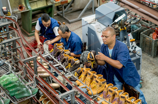 Group of men working at a shoe making factory - manufacturing industry concepts