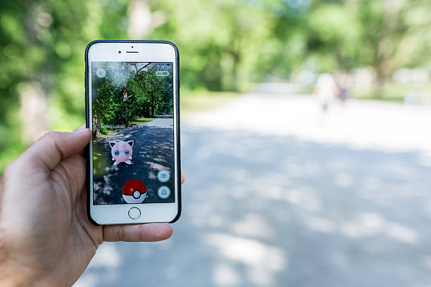 Terrebonne, Сanada - August 1, 2016: Human Hand holding an Apple Iphone and playing Pokemon Go while walking in the Parc des Vieux Moulins, Terrebonne, Quebec. Pokemon Go is a popular location based augmented reality mobile game.