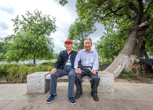 Jilin, Сhina - June 25, 2016: Two elderly Asian men sitting on the stone bench in Jilin Beishan Park ,smiling to the photographer to take their picture.