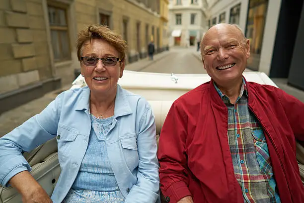 very happy laughing senior couple going with horse drawn carriage through inner city streets of Vienna during their sightseeing tour
