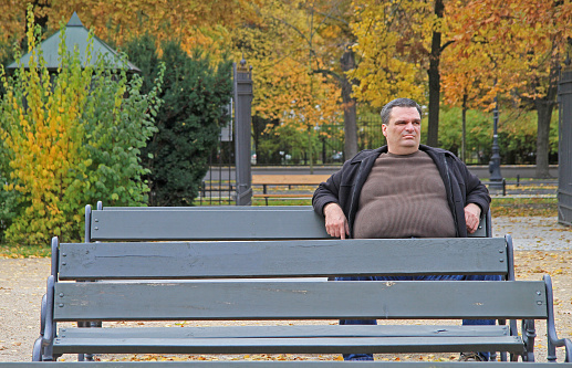 Warsaw, Poland - October 23, 2015: fat man is sitting on a bench in park of Warsaw, Poland