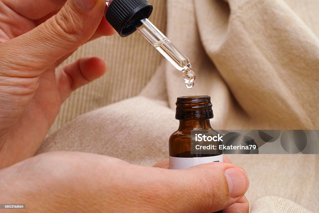 Pipette and oil bottle in woman hands Pipette with drop of essential oil and bottle in woman hands on beige textile. Aromatherapy Oil Stock Photo