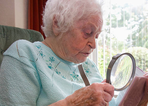 istock Elderly woman using a magnifier to read a book 585317302
