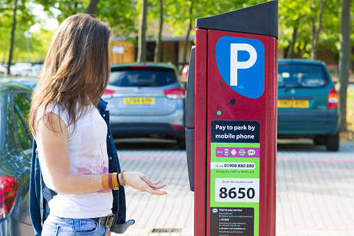 Milton Keynes, England - July 27, 2016: Female customer paying for parking the car using installed machine outdoors, UK