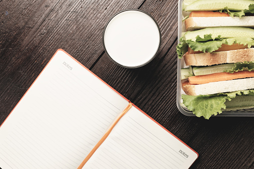Lunch box with sandwich bread and fresh vegetables and glass of  alternative milk beverage on dark wood background. Concept of healthy dining out.