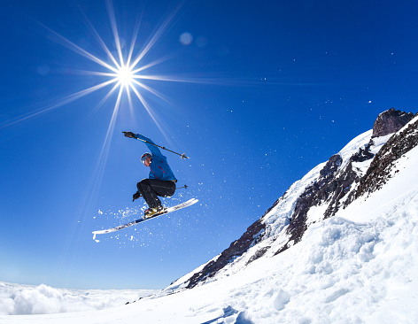 A back-country skier launches off a jump on the Muir Snowfield on Mt. Rainier, Washington State. Sunstar is authentic from original image. 
