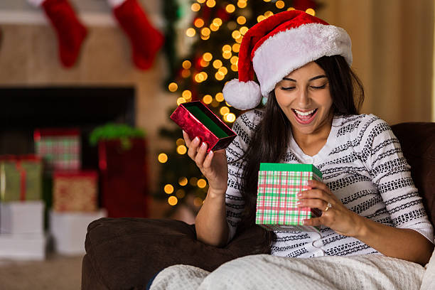 une jeune femme surprise ouvre un cadeau de noël - blanket fireplace winter women photos et images de collection