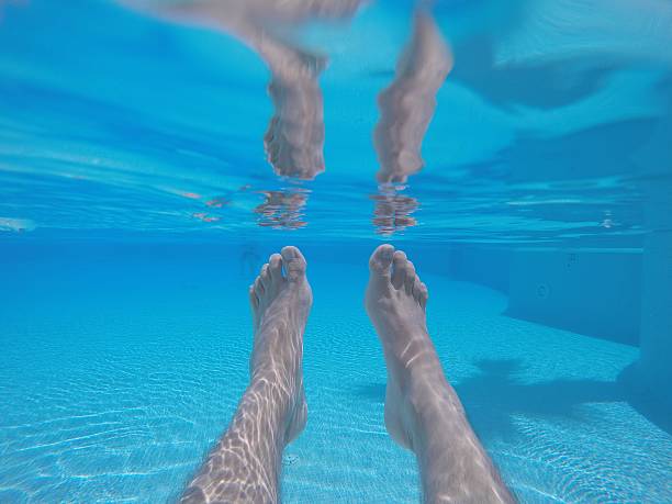 Underwater shot of male feet in blue clear swimming pool water in sunlight