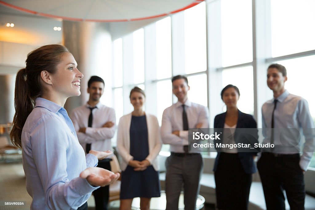 Female Executive Manager and Team Portrait of successful female executive manager with open hands gesture standing in front of her team in office hall and announce good news Number 6 Stock Photo