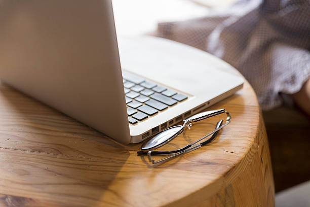 eyeglasses with laptop computer notebook on wooden desk with background of woman sitting on chair