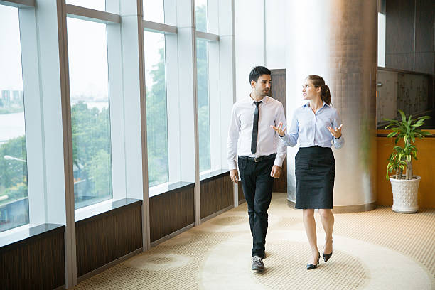 Business People Walking in Office 1 Two young female and male business people talking and walking along window in office. Woman is gesturing and smiling. white shirt black skirt stock pictures, royalty-free photos & images