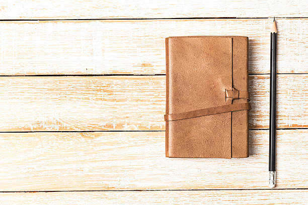 istock Leather diary notebook with pencil on white wooden background, 585492138