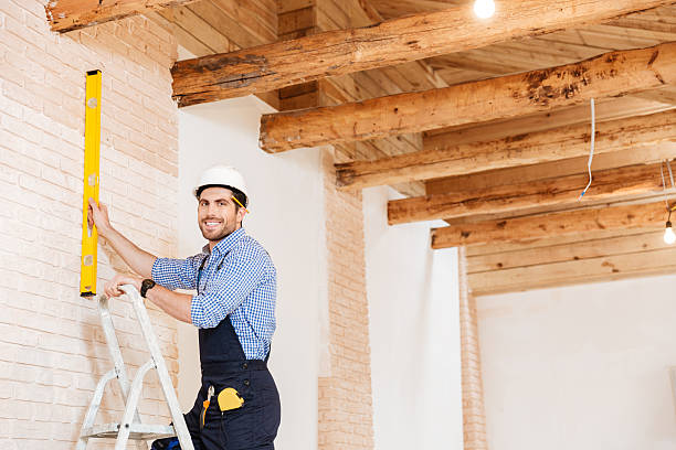 istock Smilling handsome builder using level and standing in the ladder 585503368