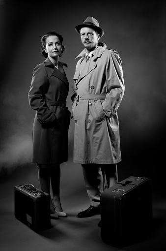 Film noir: elegant couple ready to leave with luggage waiting with hands in pockets
