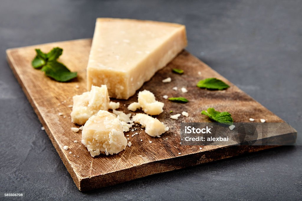 Piece of a parmesan and grated cheese Pieces of parmigiano reggiano or parmesan cheese on wood board on stone background. Parmesan is hard cheese uses in pasta dishes, soups, risottos and grated over salads. Parmesan Cheese Stock Photo