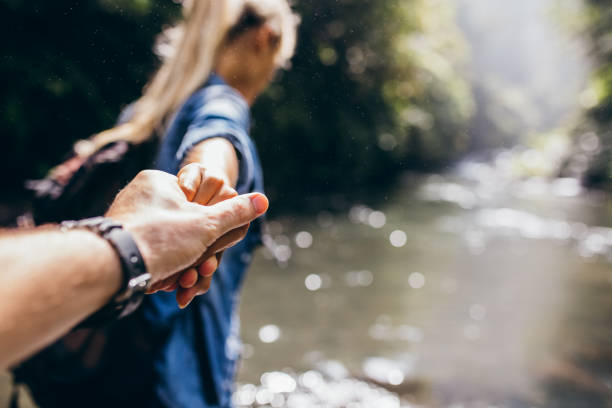 Two hikers in nature crossing the stream holding hands
