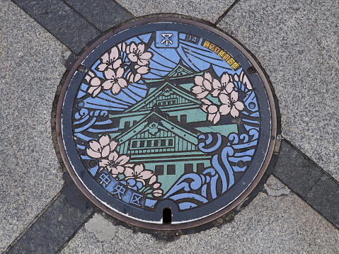 Osaka, Japan - June 07, 2016: A manhole cover in Osaka, Japan. The Osaka castle and sakura engraved on to a manhole cover as a symbol of an important city's landmark.