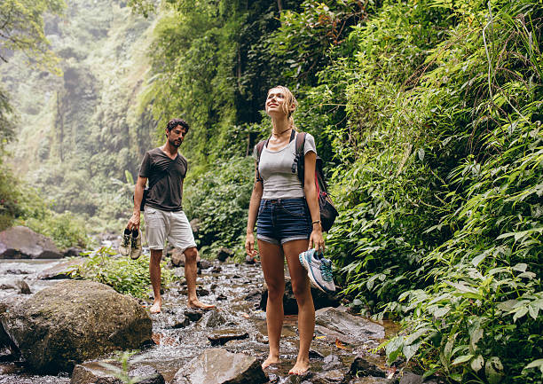 Couple across the stream. Man and woman in forest walking by a creek. Tourist on  nature hike.