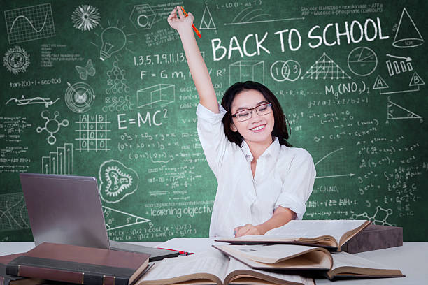 istock Girl with books raising hand in classroom 585514088