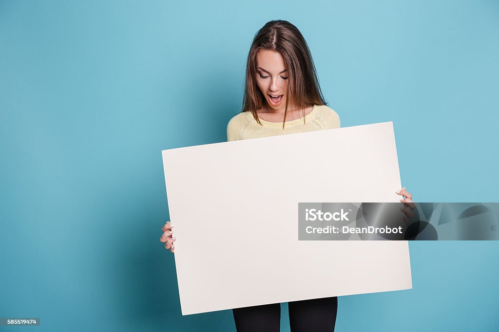 Beautiful young girl holding empty blank board over blue background Beautiful girl holding empty blank board isolated on the blue background Sign Stock Photo