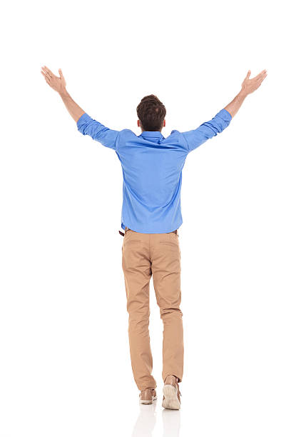Rear view of a young casual man Rear view of a young casual man holding his hand up, celebrating a victory. arms outstretched stock pictures, royalty-free photos & images