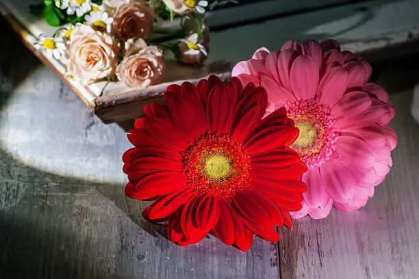 Still life with gerbera, roses and daisies in front of a picture frame on a wooden table