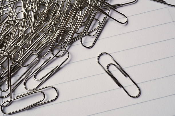 istock Heap of metal paper clips on white lined paper notepad 585524738