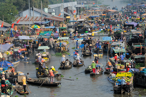 Cantho, Vietnam - January 25, 2014: The Cai Rang Floating Market, the largest wholesale floating market in the Mekong Delta, starts around 05:00 and runs until around midday. The market is about six kilometres from Can Tho, or about a 30-minute boat ride. While floating down the river, you will glimpse life along its shores. You’ll pass vibrantly painted boats anchored along the shore, merchant vessels carrying loads down the river and houses built on stilts over the water.