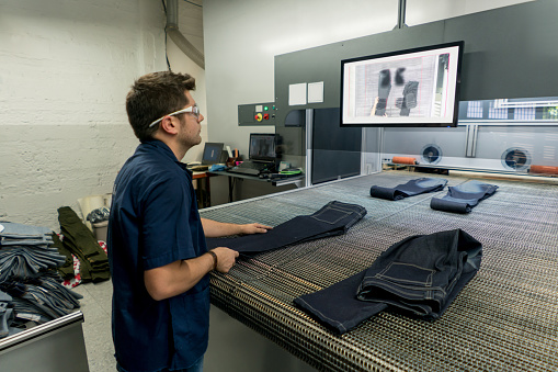 Man operating a laser machine ripping jeans at a clothing factory - textile industry concepts