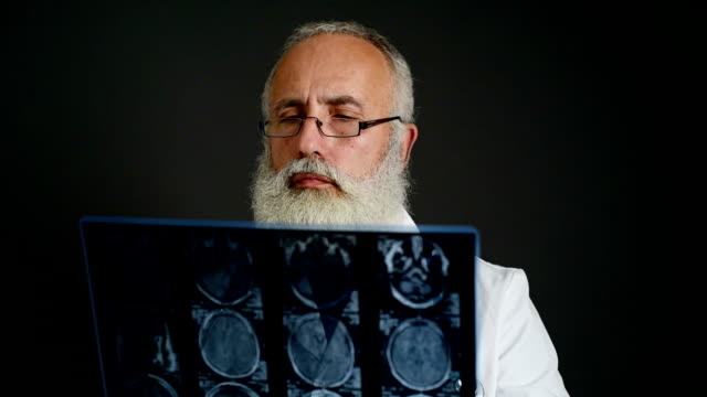 adult senior doctor looks picture MRI of the head on a dark background