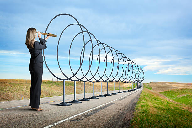 istock Businesswoman Looking Through Spyglass Down Road Lined With Hoops 585582442