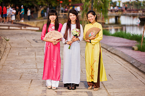 Three young Vietnamese women  wearing ao dai, Hoi An, Vietnam. Hoi An is situated on the east coast of Vietnam. Its old town is a UNESCO World Heritage Site because of its historical buildings.