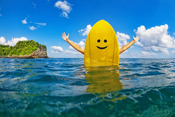 szczęśliwa dziewczyna surfer siedzieć na żółtej desce surfingowej z buźką - summer camp sign child summer zdjęcia i obrazy z banku zdjęć