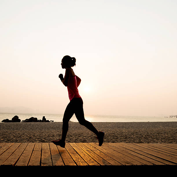 istock Woman jogging on shore at sunrise 585591570