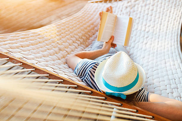 Man in a hammock with book on summer day Lazy time. Man in hat in a hammock with book on a summer day hammock stock pictures, royalty-free photos & images