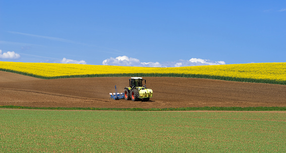 Tractor during sowing among fields in hilly landscape in spring 
