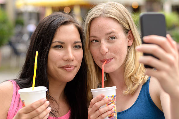 istock Cute women with beverages taking self portrait 585604890