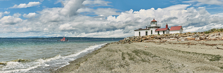A very large stitched panorama of West Point Light, built in 1881 and located in Discovery Park in Seattle, Washington. A tugboat is chugging by on Puget Sound in the background.