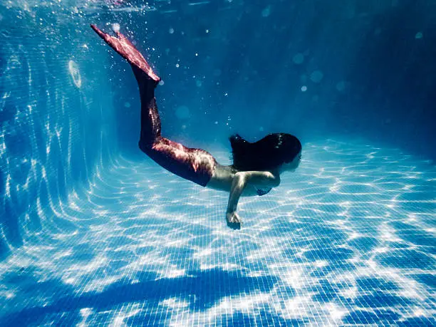 A girl in a mermaid costume swimming underwater in pool