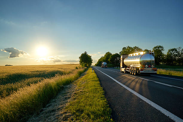 Trucks with chrome tank driving on road at sunset. Trucks with chrome tank driving on asphalt road along the corn field at sunset. The landscape and the road are mirrored on a silver tanker. fuel truck photos stock pictures, royalty-free photos & images