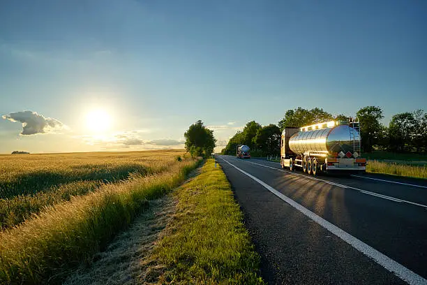 Photo of Trucks with chrome tank driving on road at sunset.