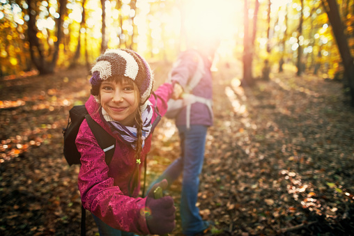 Happy mother and daughter hiking in the forest in the autumn. The girl and mother are having fun and holding hands. The girl is smiling at the camera.