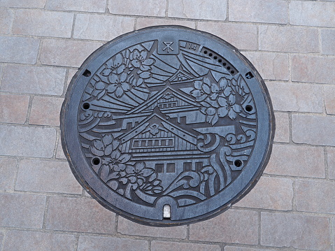 Osaka, Japan - June 08, 2016: A manhole cover in Osaka, Japan. The Osaka castle and sakura engraved on to a manhole cover as a symbol of an important city's landmark.