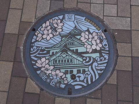 Osaka, Japan - June 09, 2016: A manhole cover in Osaka, Japan. The Osaka castle and sakura engraved on to a manhole cover as a symbol of an important city's landmark.