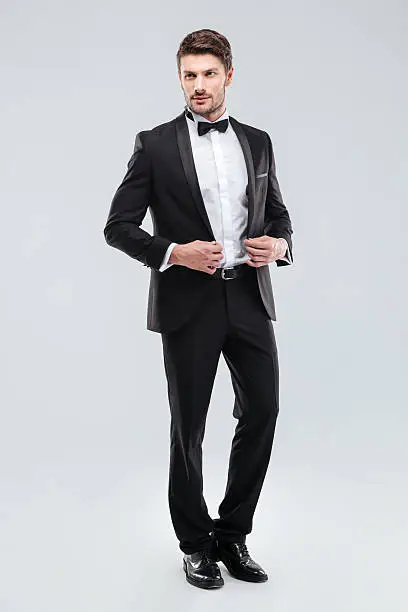 Full length of handsome young man in tuxedo with bowtie standing