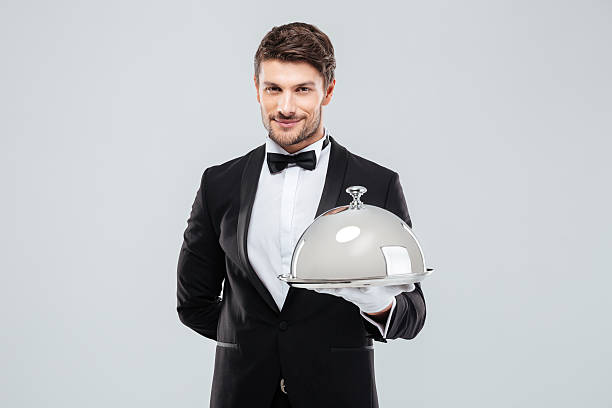 istock Smiling young butler holding tray with silver catering dome 585768514