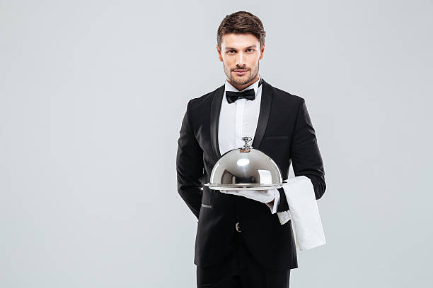 istock Waiter in tuxedo holding serving tray with cloche and napkin 585768708